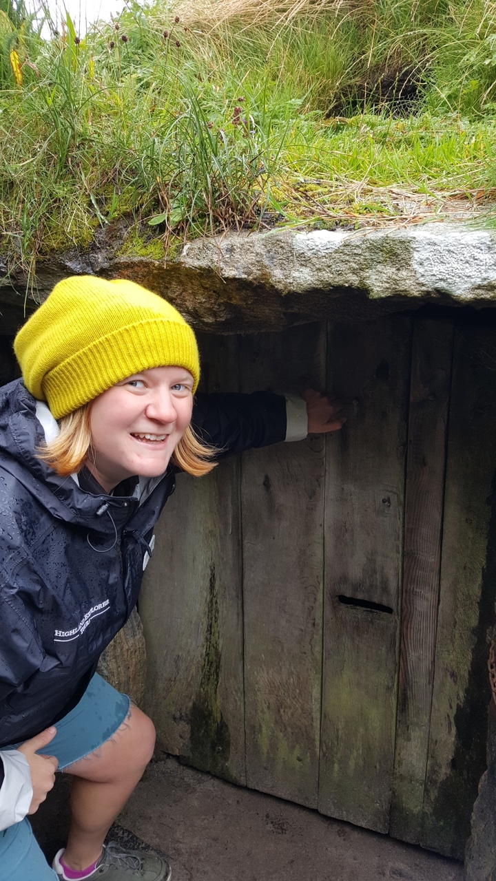 Personne souriante avec un chapeau jaune près d'un mur en bois.