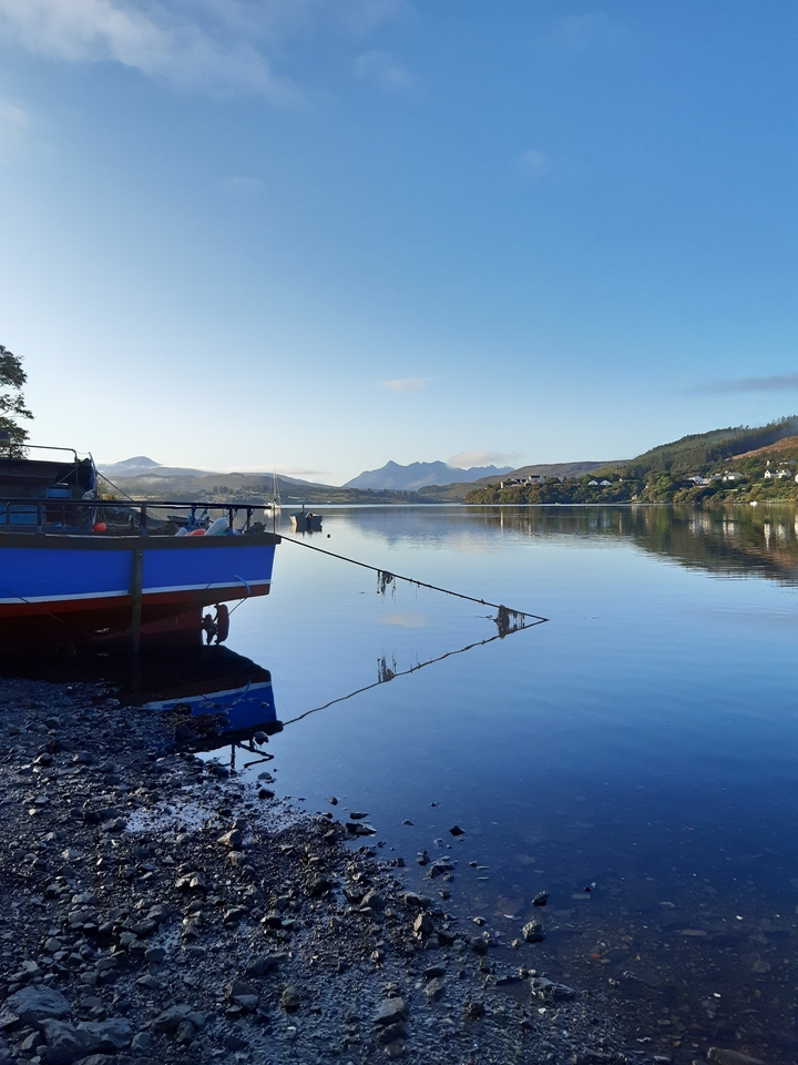 Bateau amarré sur un lac tranquille avec des montagnes en arrière-plan.