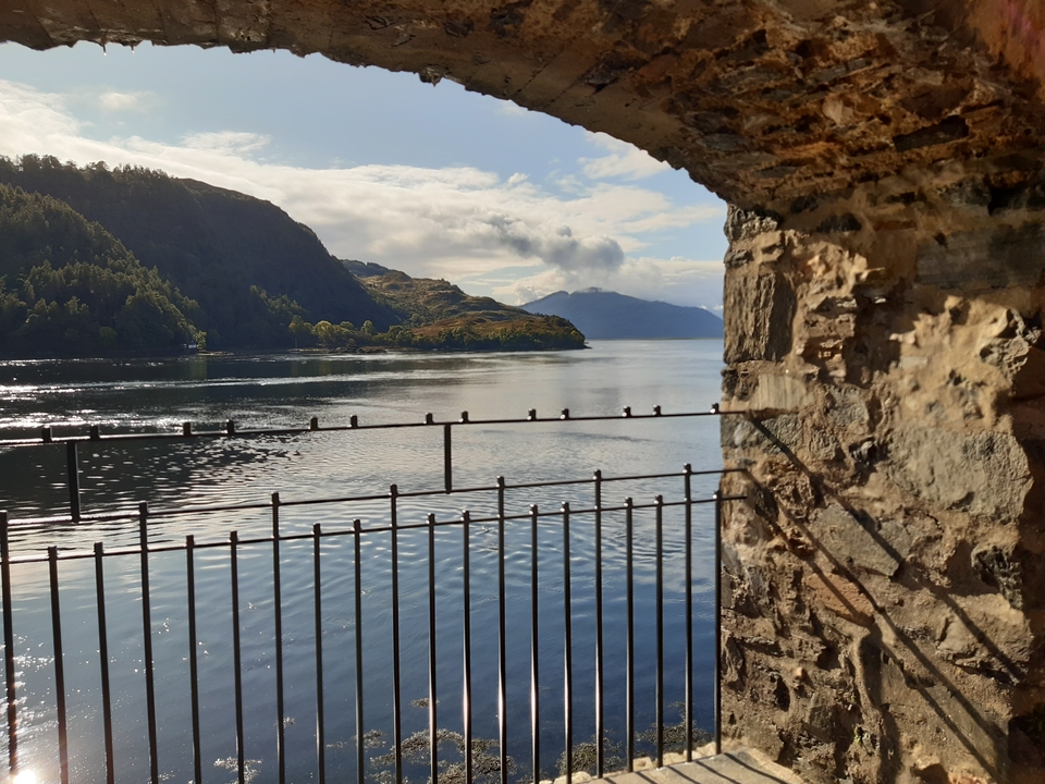 Vue d'un lac à travers des ruines de pierre avec des montagnes.