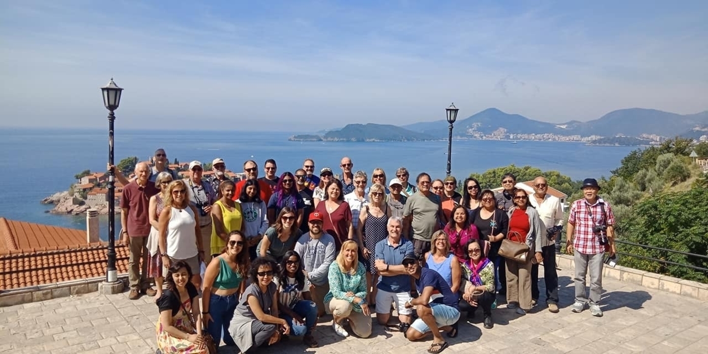 Grand groupe posant avec les montagnes et la mer en arrière-plan.
