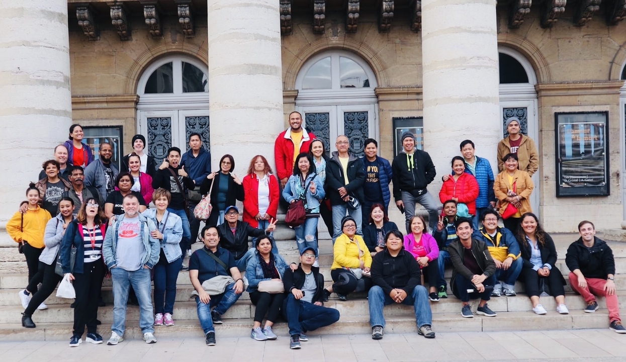 Photo de groupe de personnes assises sur des marches devant un bâtiment.