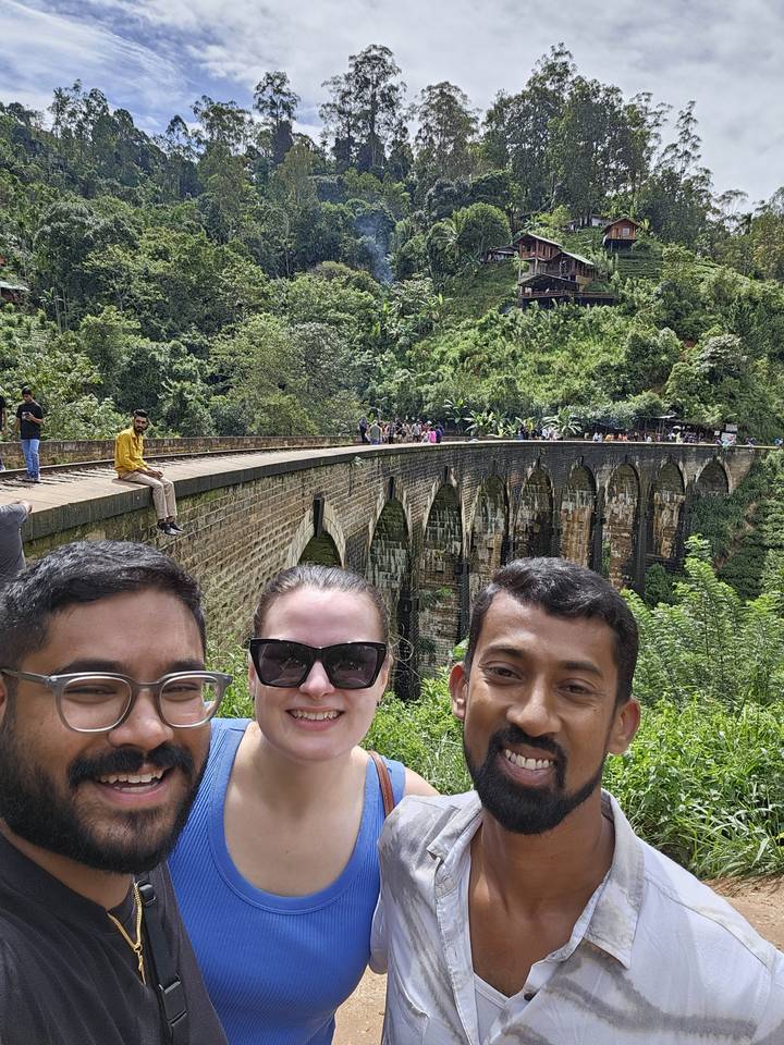 Trois personnes prenant un selfie avec de la verdure et des structures en pierre en arrière-plan.