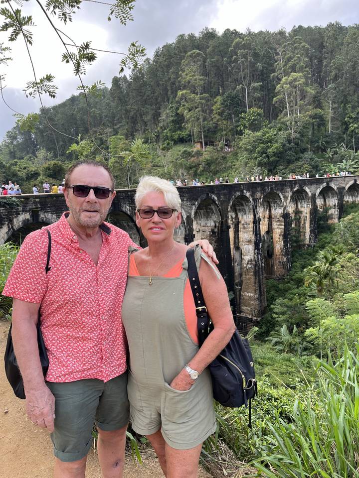 Deux personnes posant avec un viaduc ferroviaire pittoresque en arrière-plan.
