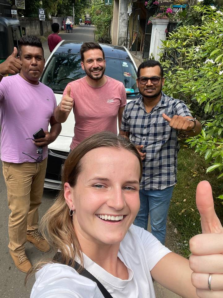 Groupe d'amis souriants prenant un selfie avec de la verdure en arrière-plan.