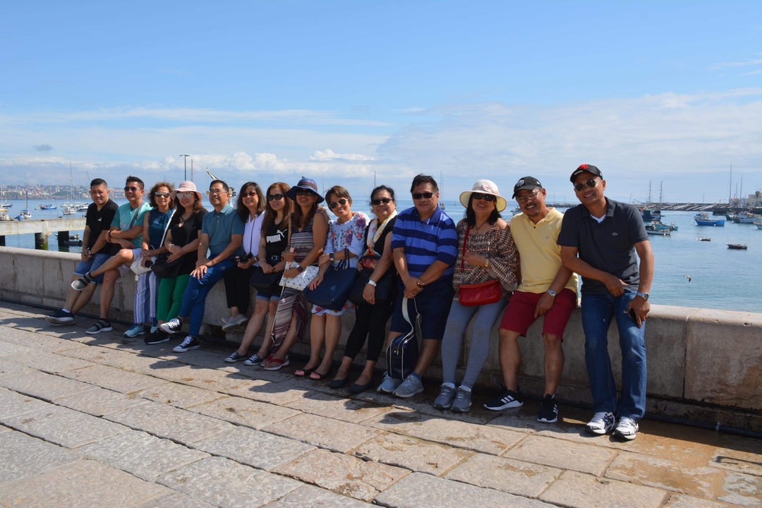 Des gens assis sur un mur en bord de mer avec des bateaux en arrière-plan.