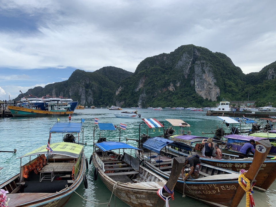 Busy pier filled with boats and vibrant scenery of towering cliffs.