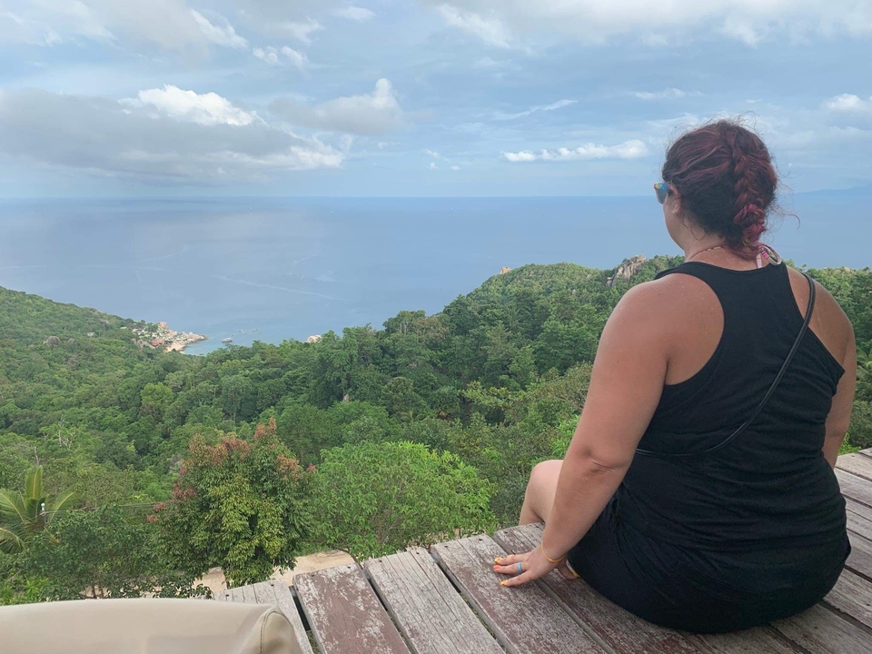 Person sitting on a wooden platform overlooking a vast ocean view.