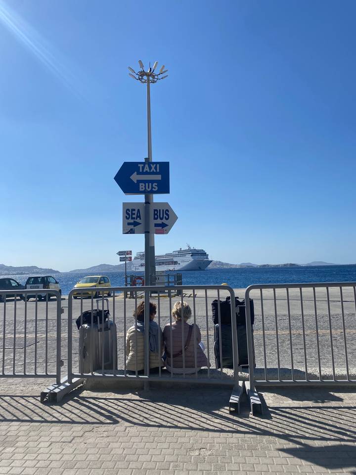 Des gens qui attendent à un arrêt de navette maritime avec un navire de croisière en arrière-plan.