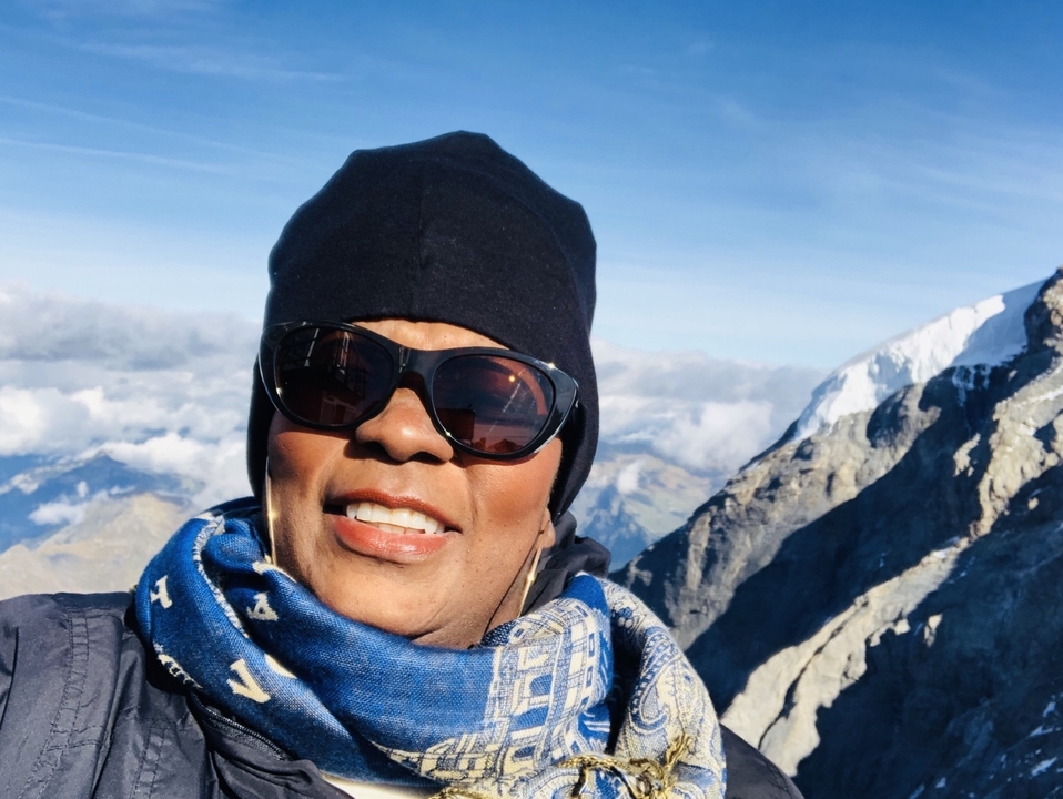 Personne qui pose avec des lunettes de soleil sur un arrière-plan de montagne.
