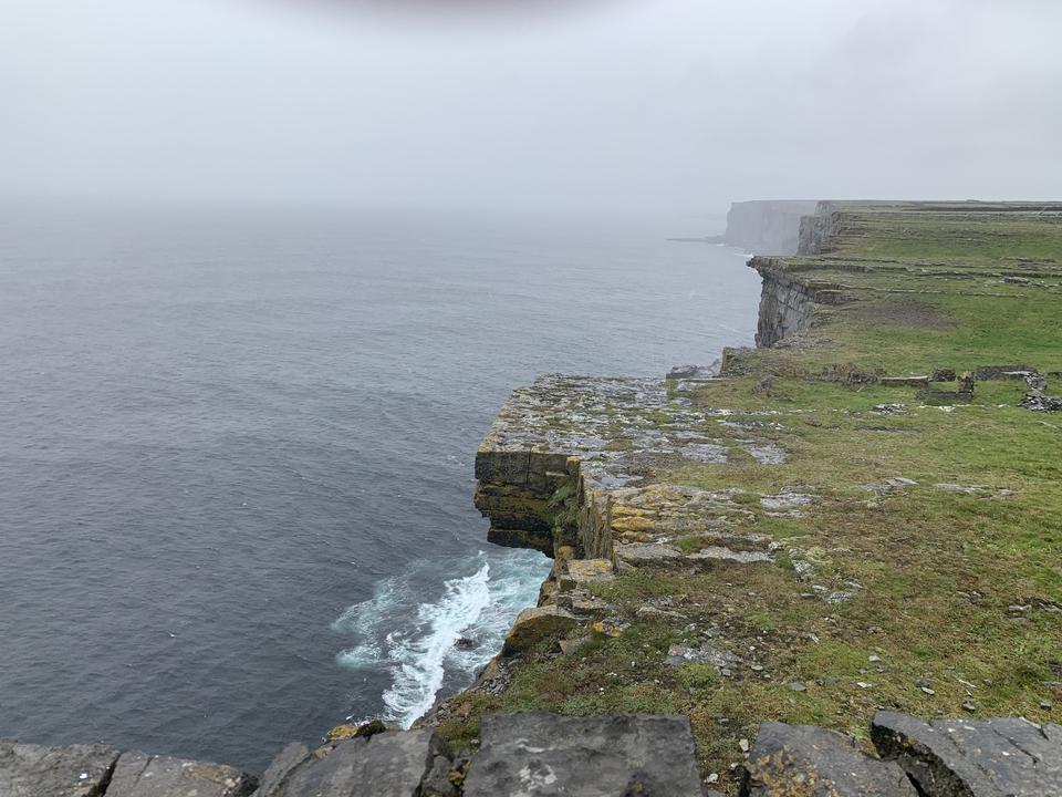 Mer agitée en contrebas de hautes falaises par temps brumeux.