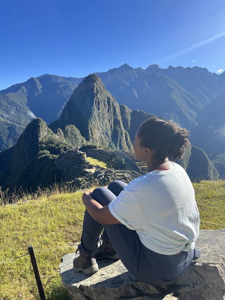 Personne assise sur un rebord rocheux surplombant un terrain montagneux.