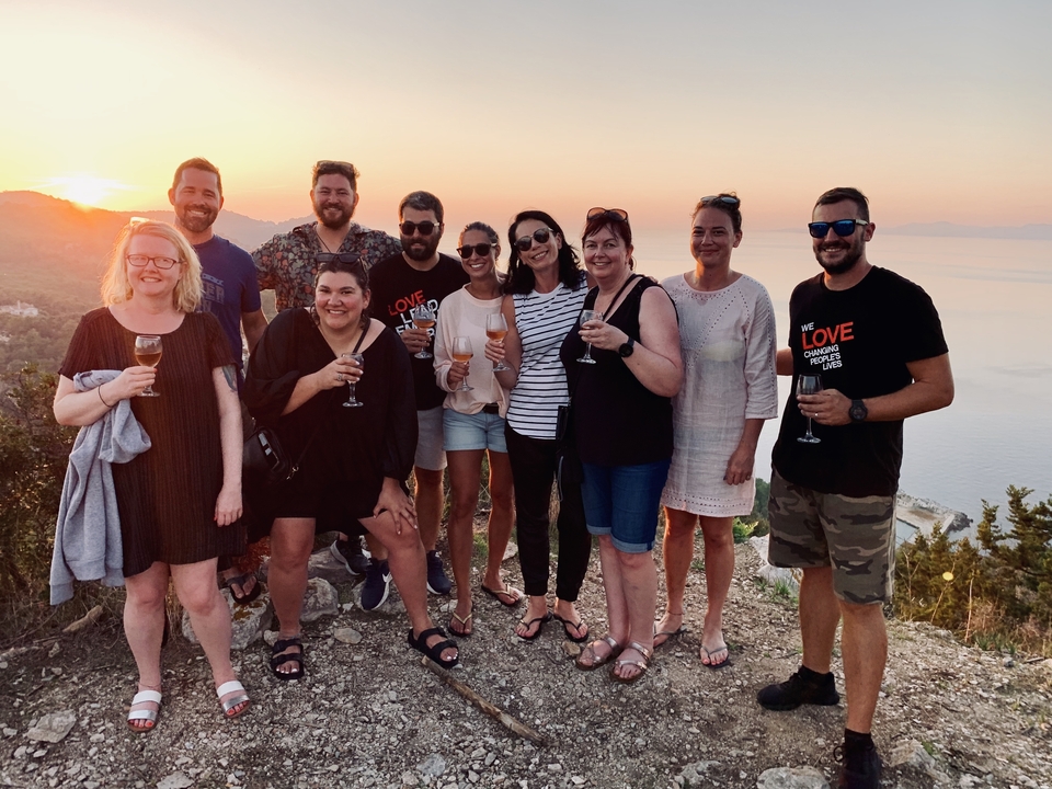 Groupe de personnes avec des boissons au coucher du soleil avec vue sur la mer.