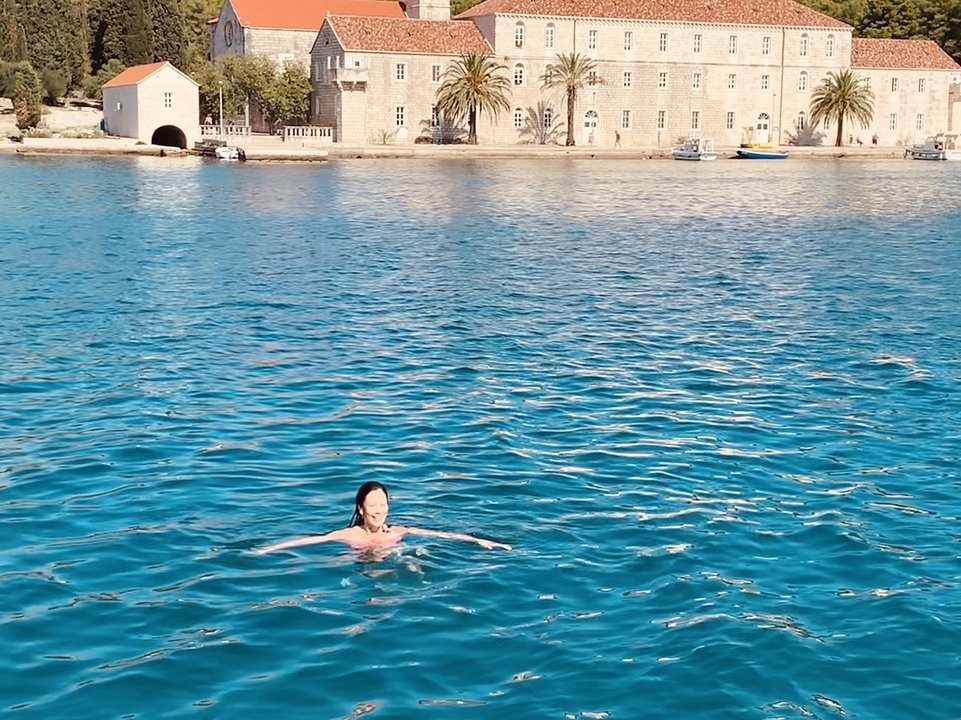 Personne nageant dans des eaux bleues claires avec des bâtiments en arrière-plan.