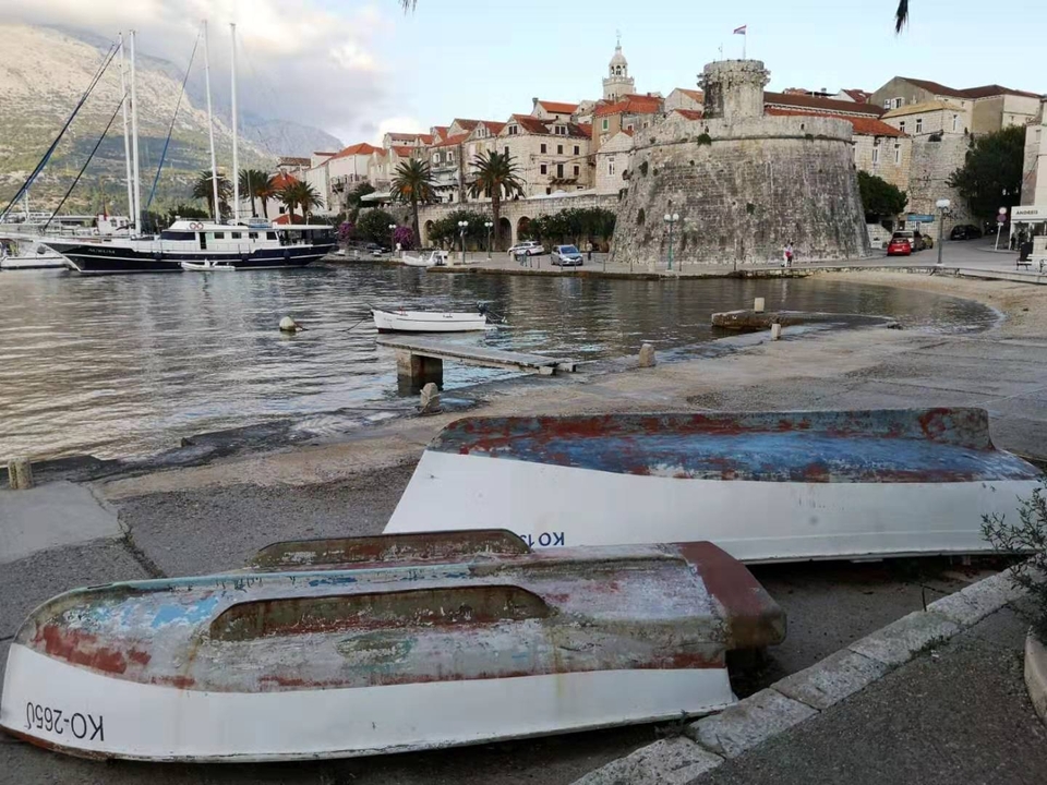 Vieux bateaux sur une plage de galets près de bâtiments historiques.