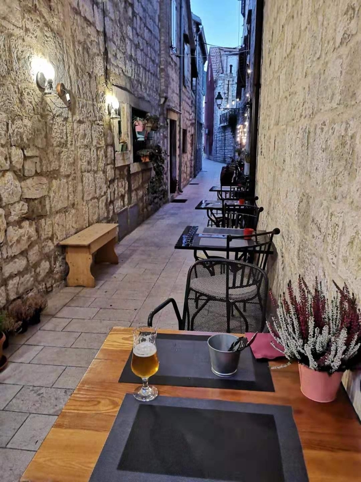 Ruelle étroite pavée de pierres avec des places de restaurant vides.