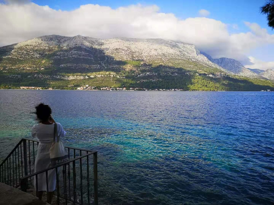 Personne debout au bord de la mer calme avec des montagnes au loin.