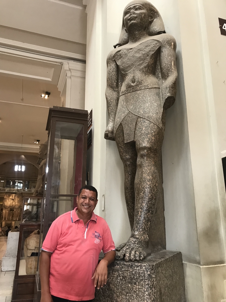 Un homme qui pose à côté d'une statue antique à l'intérieur d'un musée.
