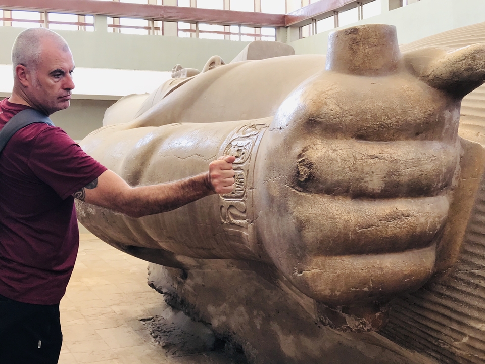 Une personne posant à côté d'une statue antique géante.