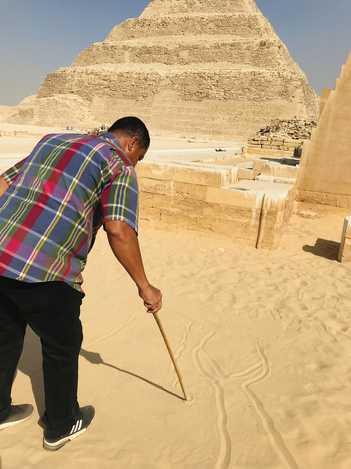 Une personne dessinant sur un sol sablonneux près de ruines.