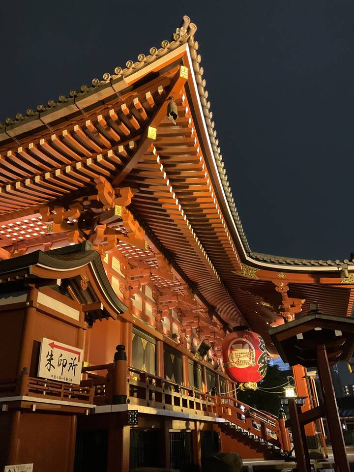 Une grande lanterne japonaise rouge dans un cadre de temple la nuit.