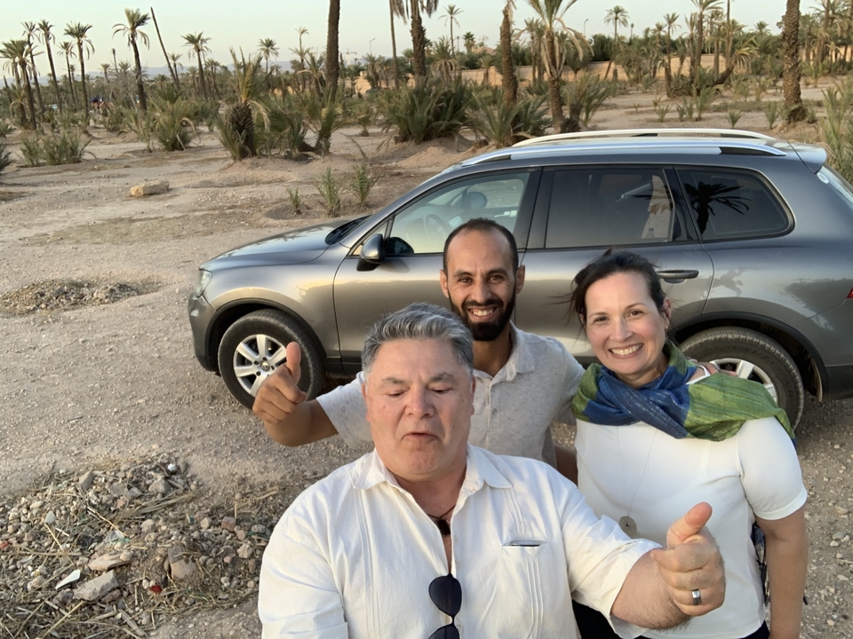 Deux personnes avec un guide et une voiture dans un décor désertique.