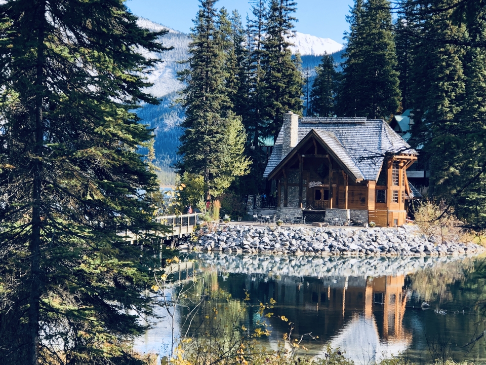 Eine malerische Hütte an einem See, umgeben von dichtem Waldbestand, der sich im Wasser spiegelt.