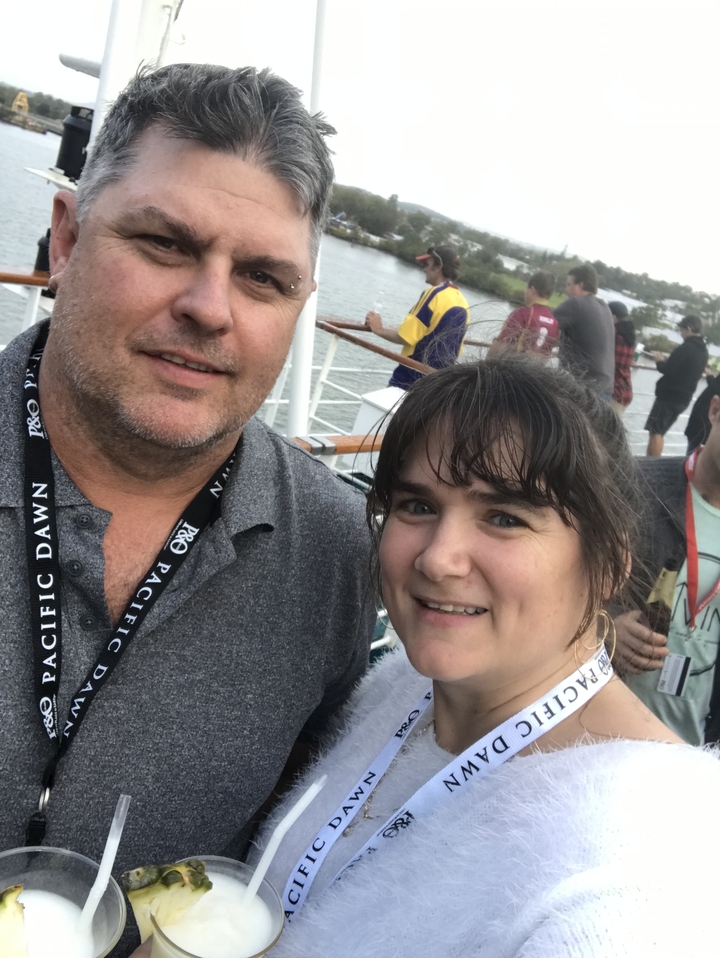 Portrait de deux personnes souriantes avec une rivière et des bateaux en arrière-plan.