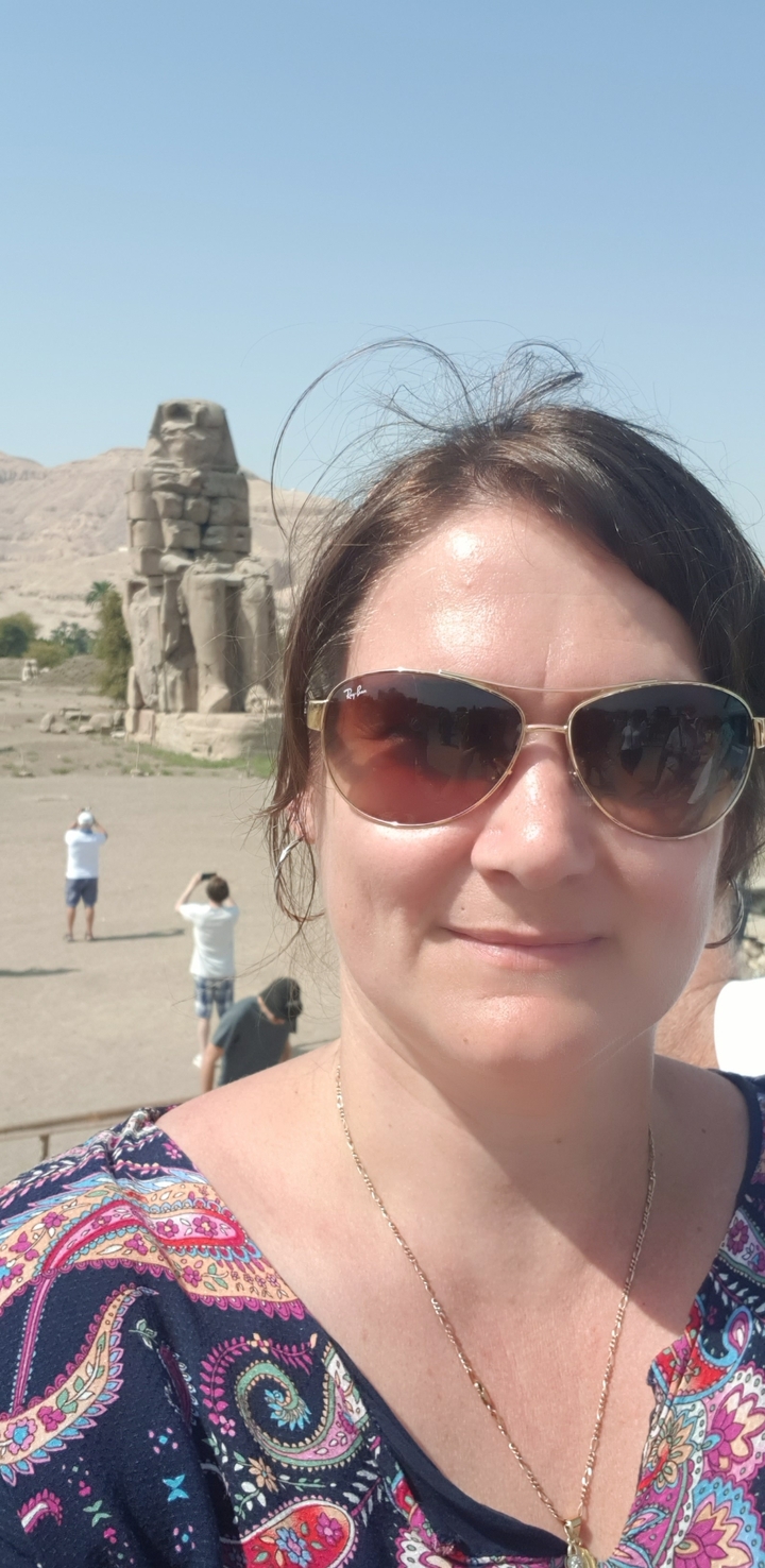 Gros plan d'une personne portant des lunettes de soleil avec des ruines antiques en arrière-plan.