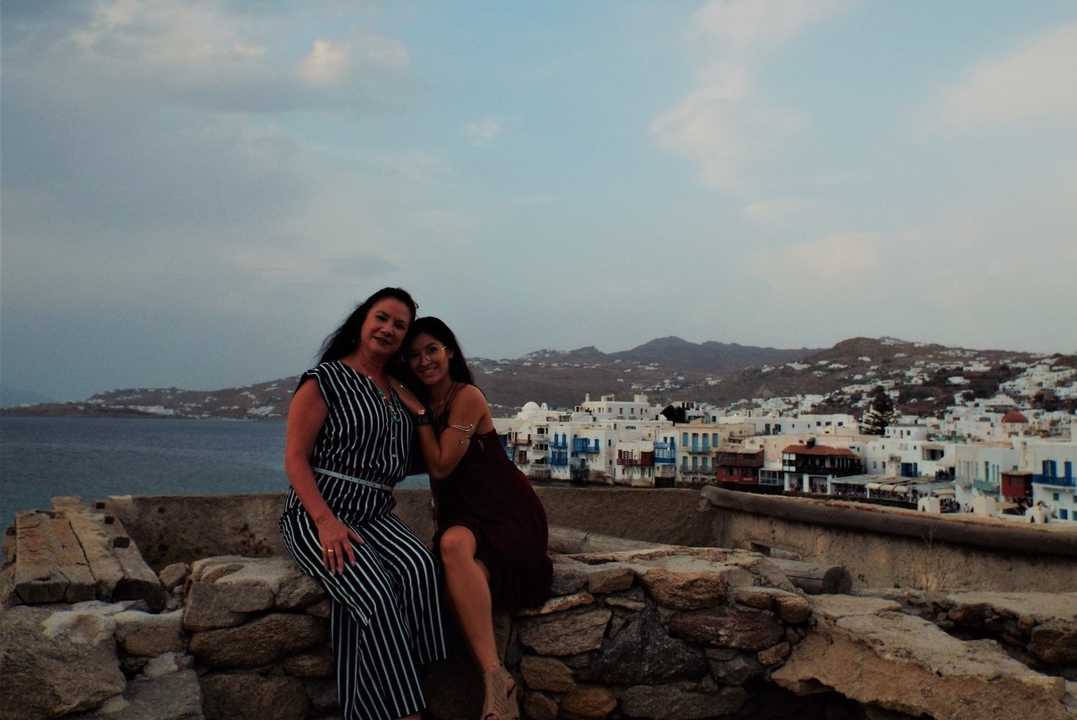 Deux femmes posant avec une vue sur des maisons blanches traditionnelles et la mer en arrière-plan.