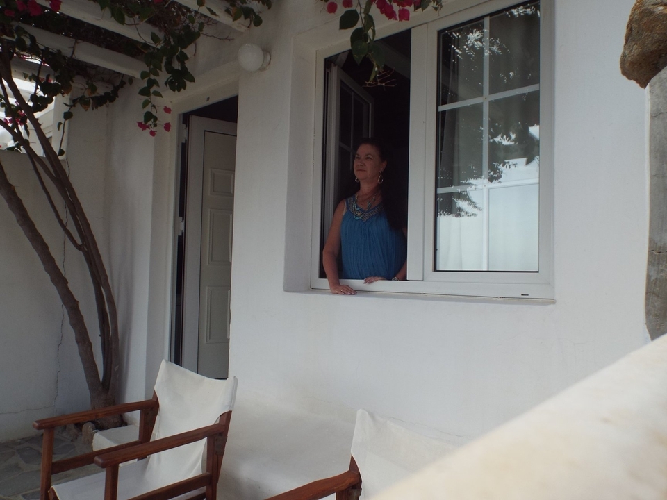 Femme regardant par la fenêtre d'un bâtiment aux murs blancs avec une expression sereine.