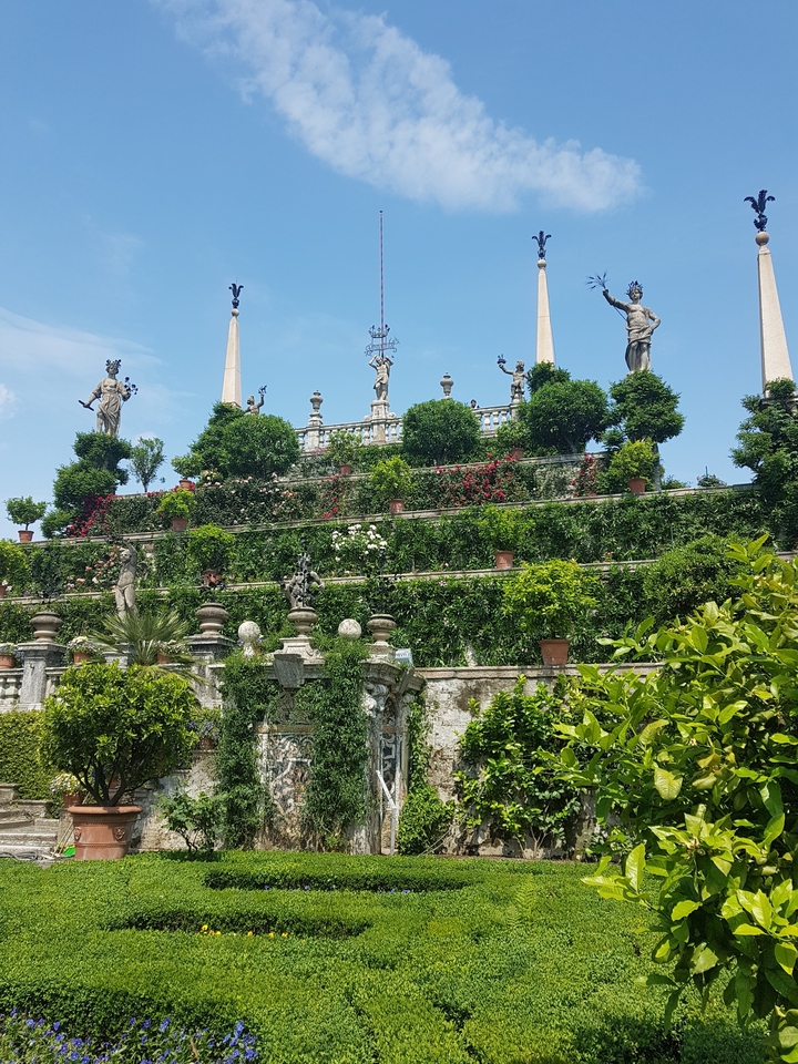 Jardin en terrasses avec statues et végétation luxuriante.
