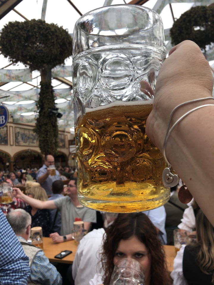 Un grand verre de bière tenu en l'air avec des gens en arrière-plan.
