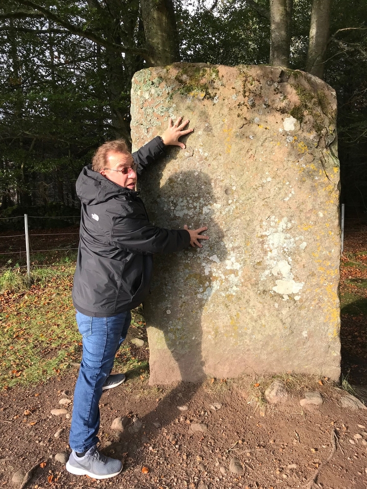 Un homme qui pose avec une grande pierre à l'extérieur.
