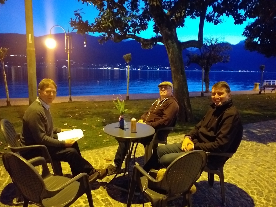 Trois hommes assis à une table de café au crépuscule au bord de l'eau.