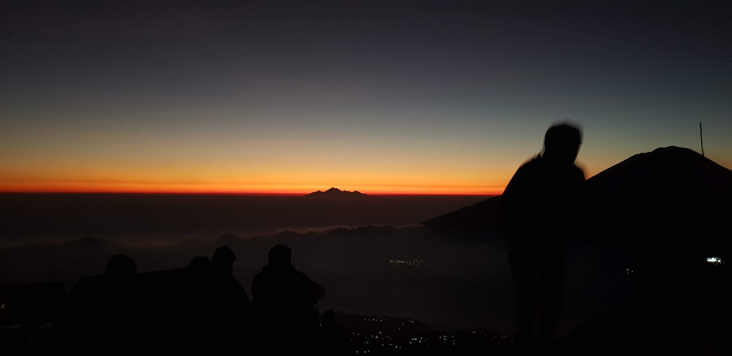Silhouette de personnes observant un lever de soleil sur des montagnes.