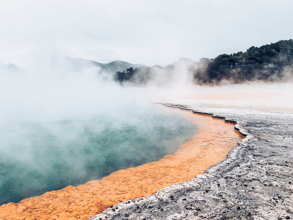 Source géothermale chaude avec brume et dépôts minéraux colorés.