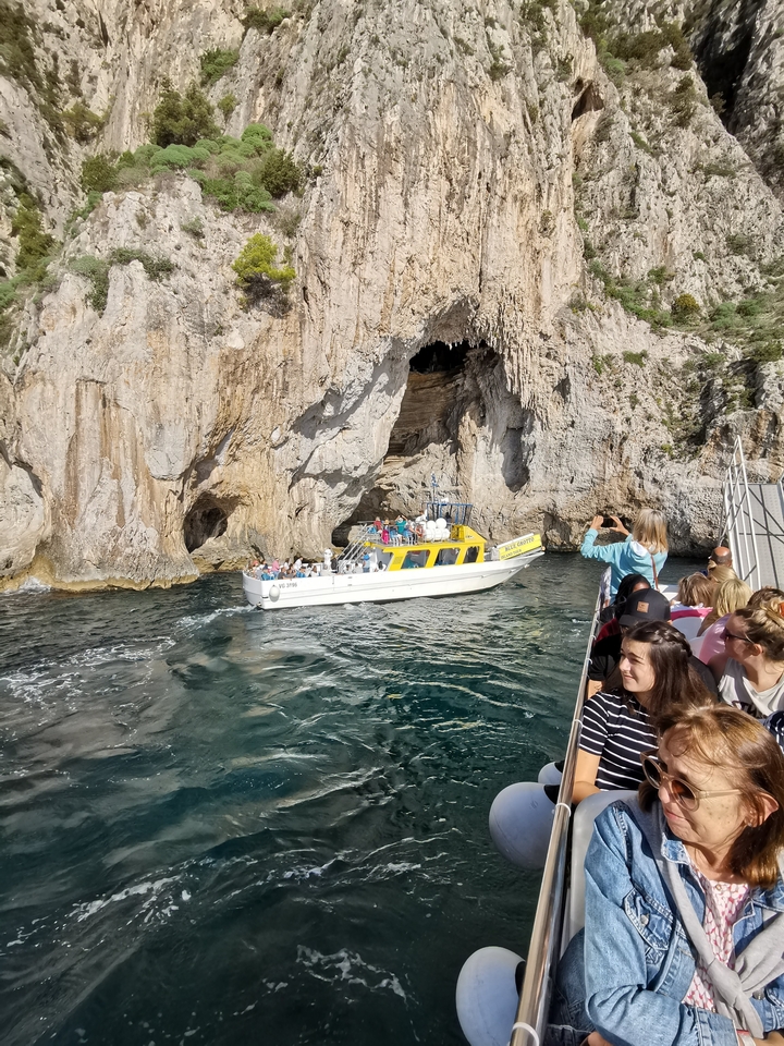 Une excursion en bateau passant devant une grotte sur une côte rocheuse avec des personnes à bord et observant les touristes