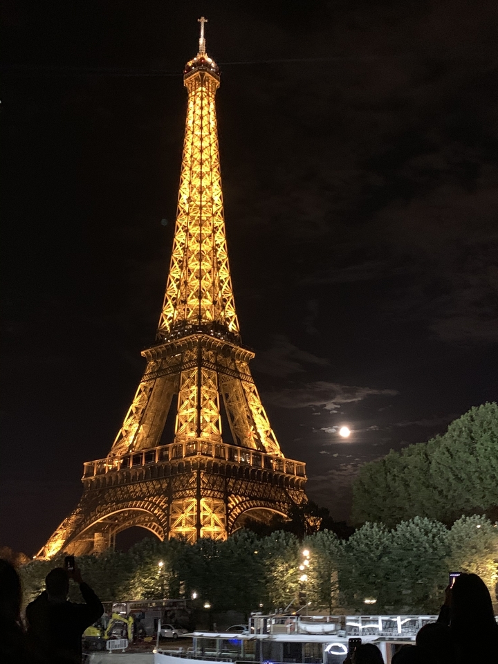 Tour Eiffel illuminée la nuit avec la lune derrière.