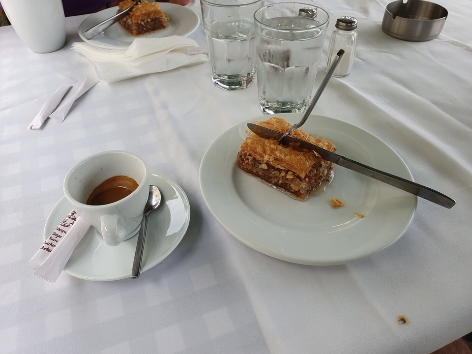 A cup of espresso and a piece of baklava with utensils on a table.