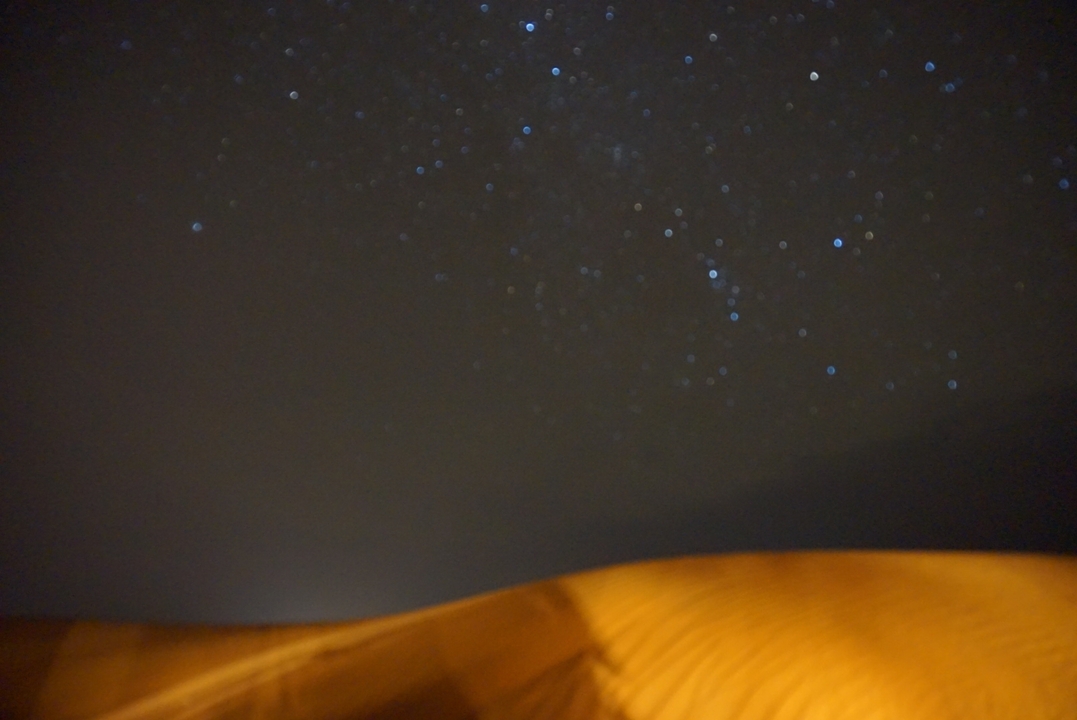 Ciel nocturne flou avec des étoiles et une dune de sable.