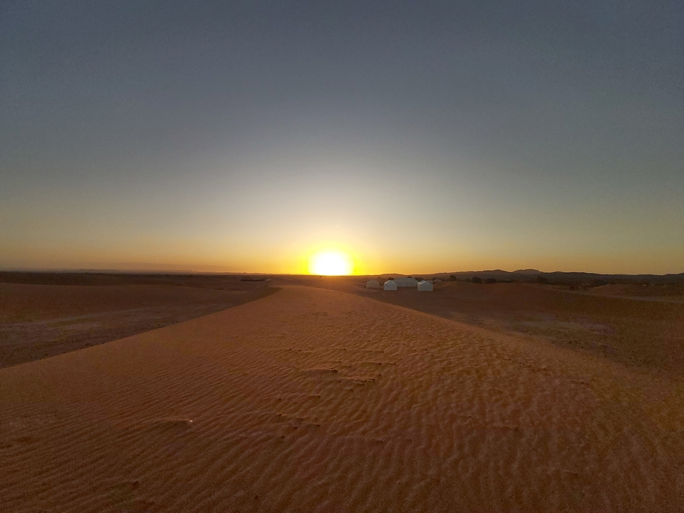 Paysage désertique au lever du soleil avec des tentes au loin.