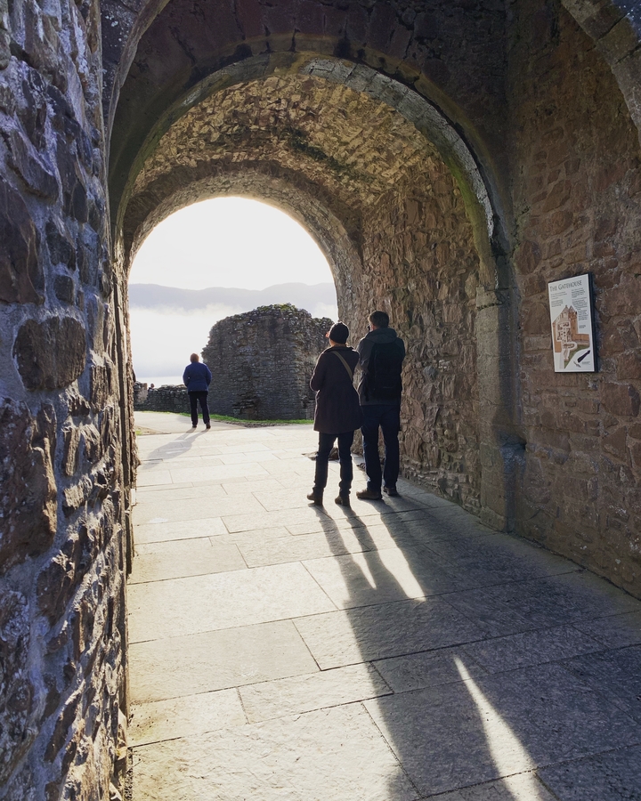 Des gens qui marchent sous une ancienne voûte en pierre avec des vues lointaines sur un loch.
