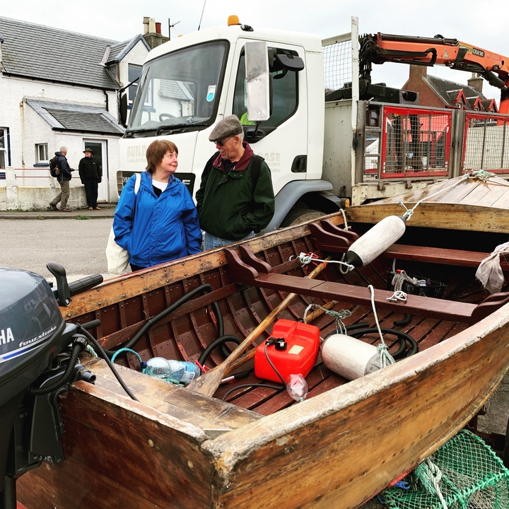 Deux personnes debout près d'un bateau en bois avec divers objets à bord.