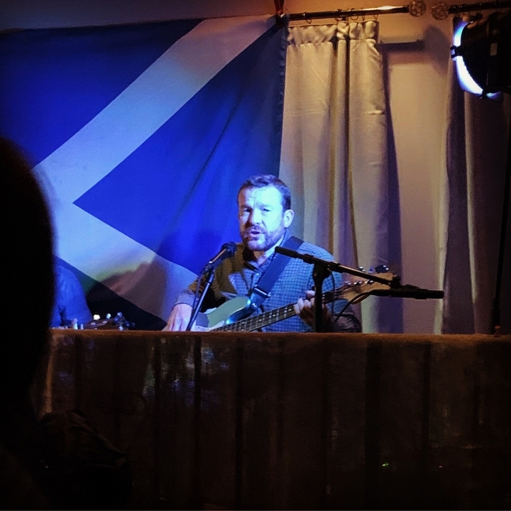 Un musicien jouant de la guitare devant un grand drapeau.