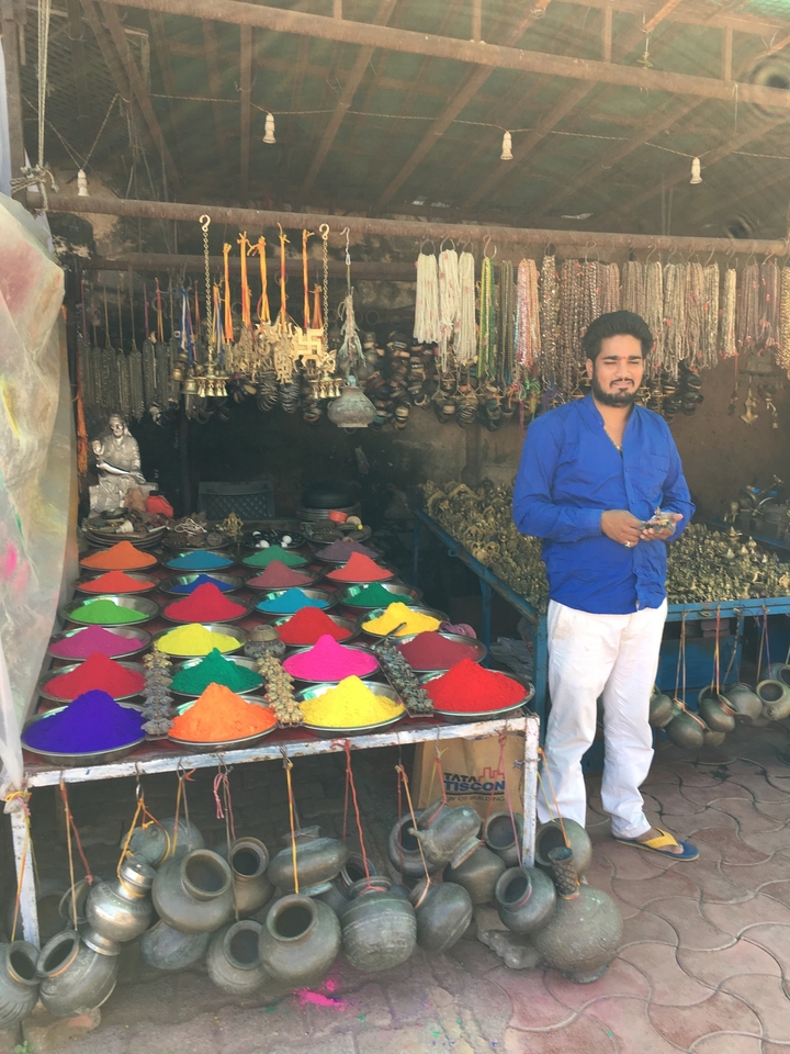Un homme en chemise bleue se tient à côté d'épices aux couleurs vives dans un marché.