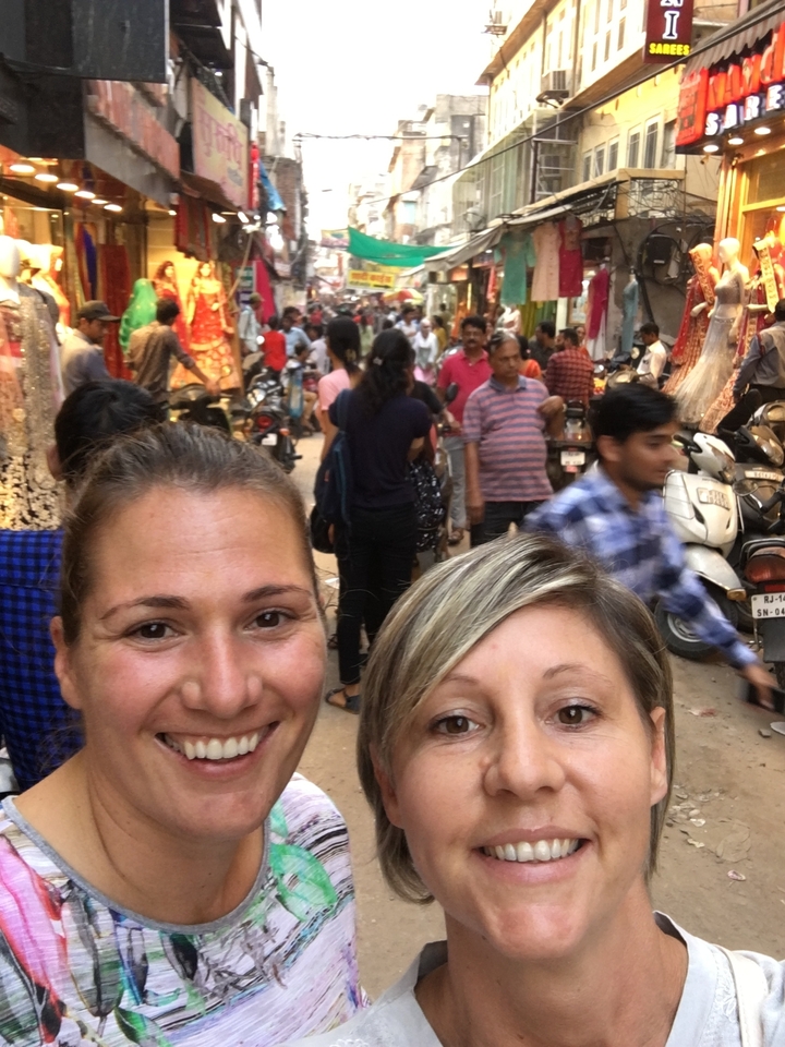 Deux personnes qui posent dans un marché animé avec beaucoup d'autres personnes autour.