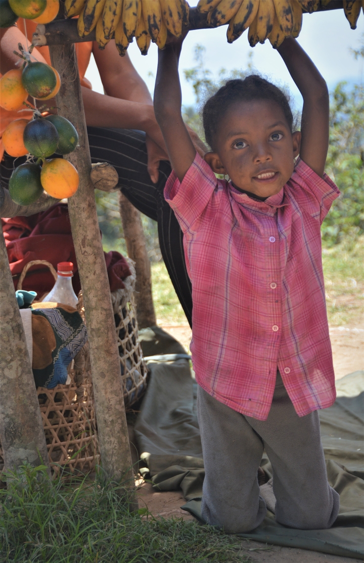 "Enfant partiellement visible avec des fruits colorés suspendus en arrière-plan."
