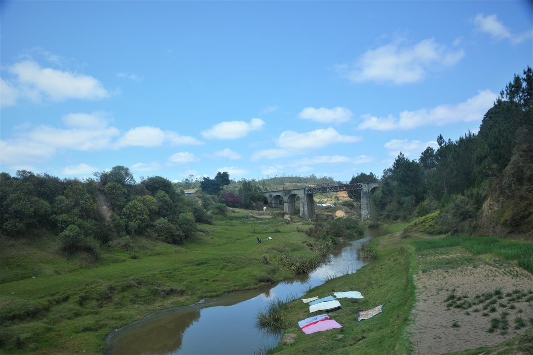 Pont sur une rivière avec un environnement verdoyant et un ciel bleu.