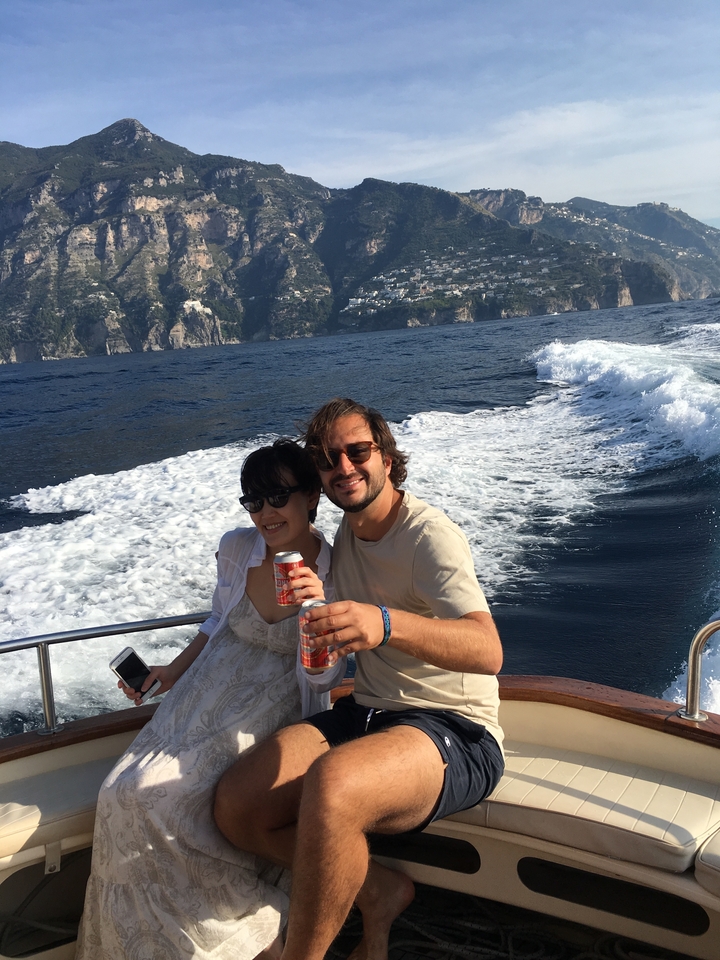 Couple souriant lors d'une promenade en bateau avec le littoral en arrière-plan.