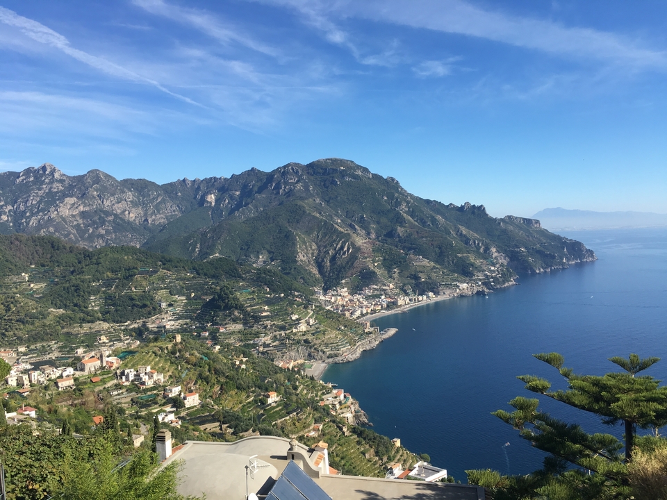 Vue majestueuse de la côte amalfitaine avec des collines vertes et une eau bleue.